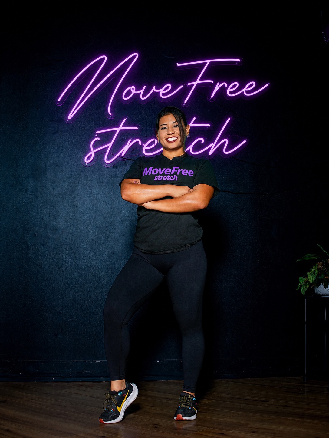 Yesenia, NASM certified personal trainer and stretch specialist, in front of the MoveFree Stretch neon sign